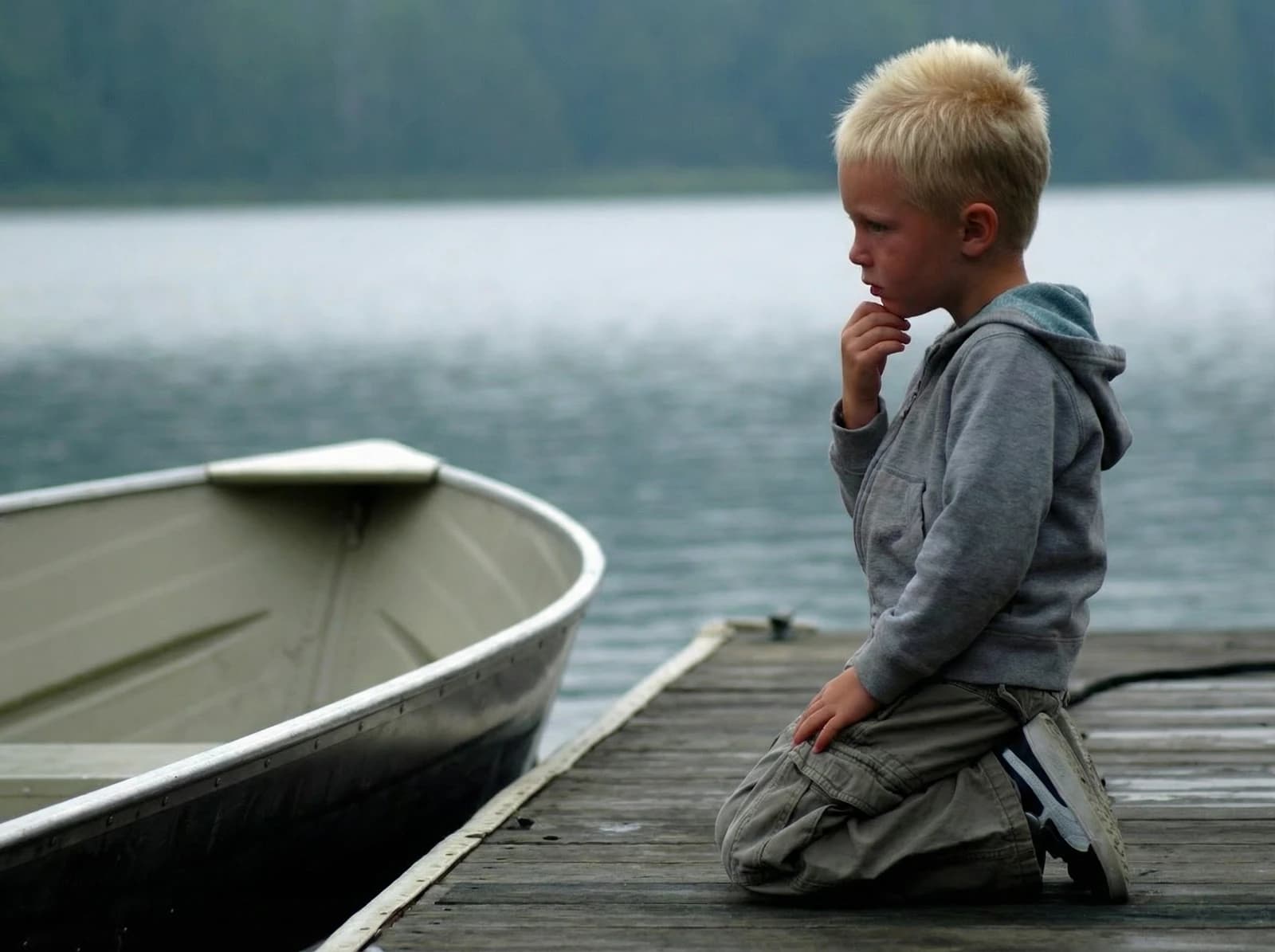 Boy on the dock beside a canoe, looking over the lake