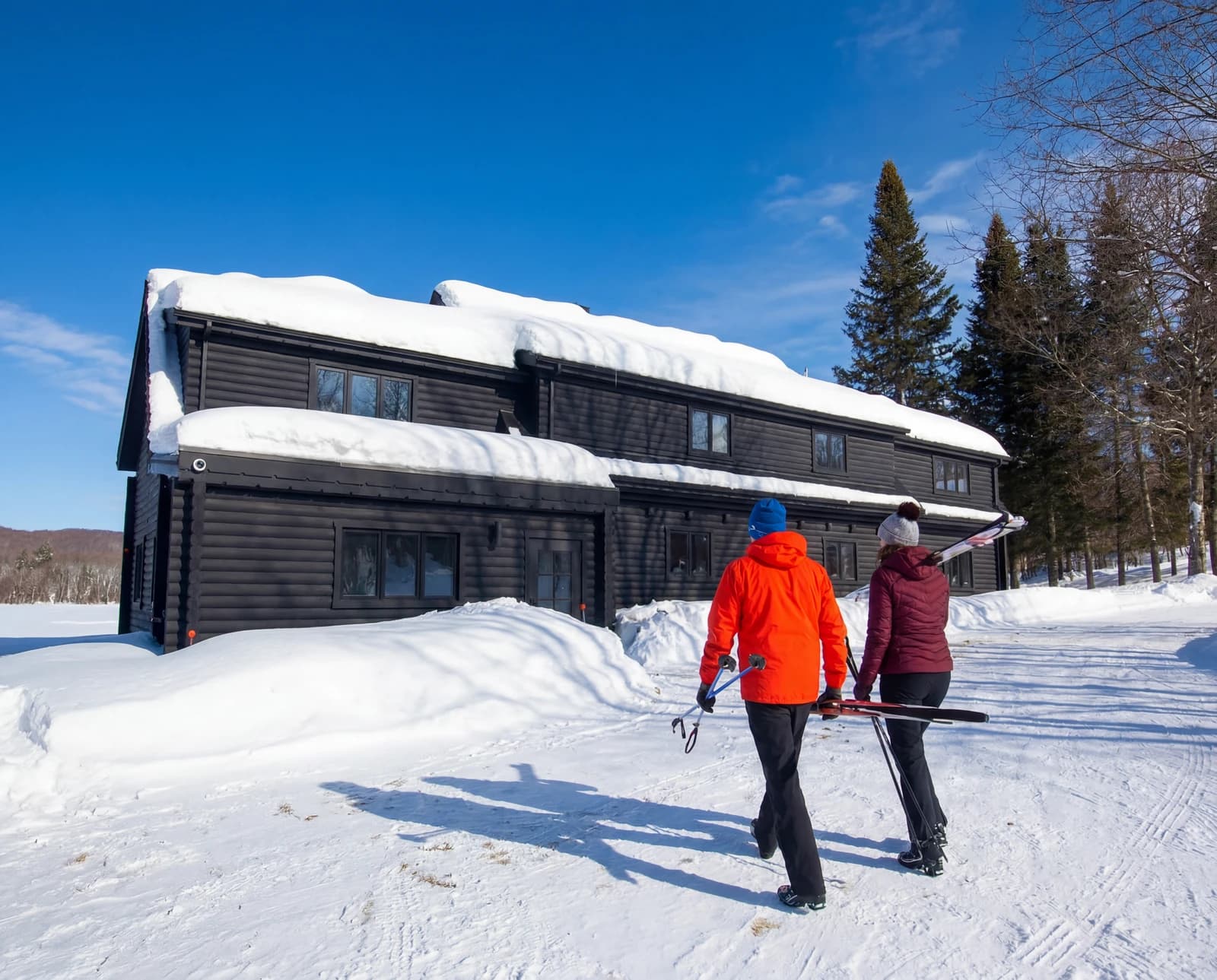 Two walkers in red crossing the snow toward the cabin