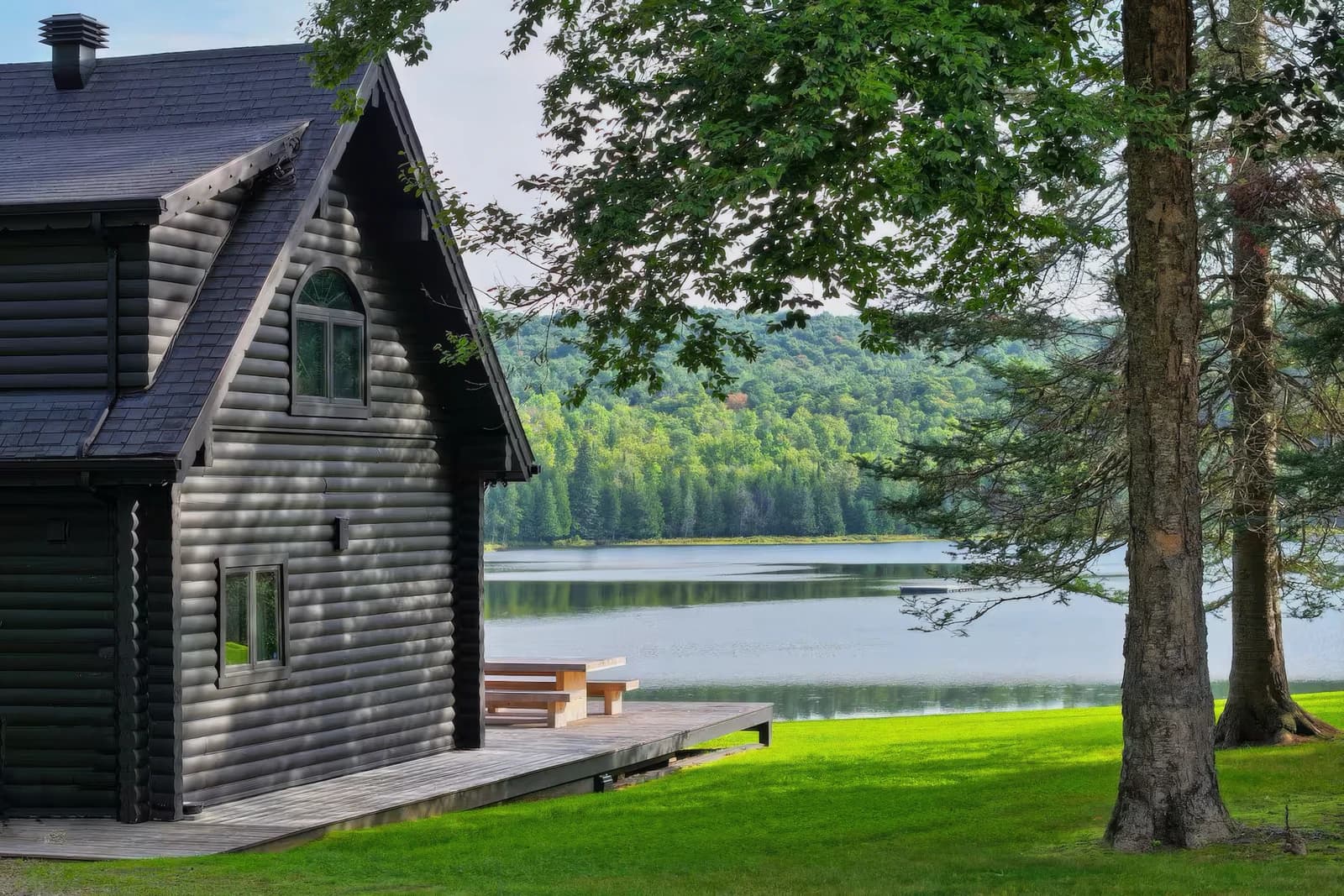 The black log residence with arched window and wooden deck, overlooking the lake and forested hills